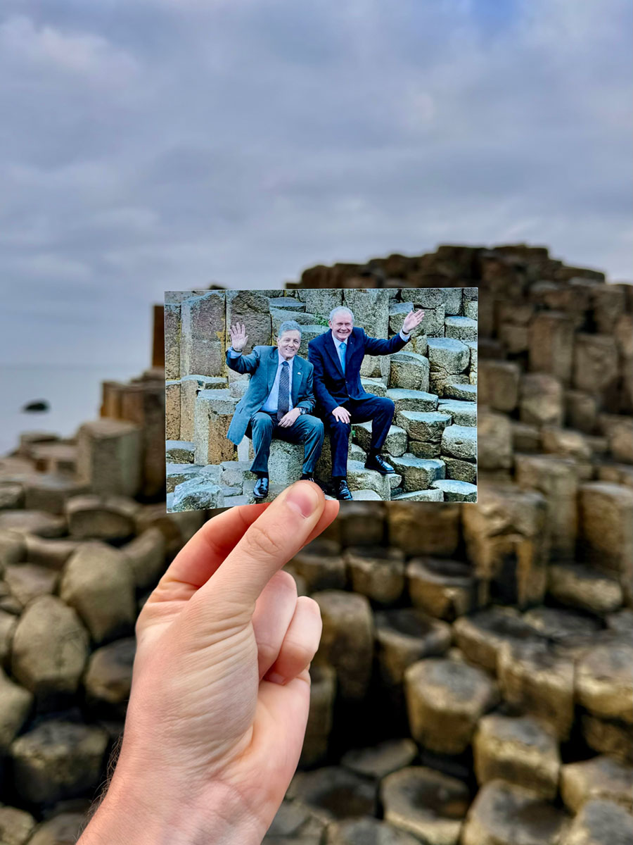 A hand holding a photograph of two men sitting on rock columns, in front of those same rock columns