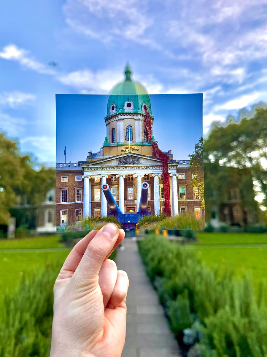 A hand holding a photograph of a domed building with an installation of red poppies flowing from a window in the roof, in front of that same building