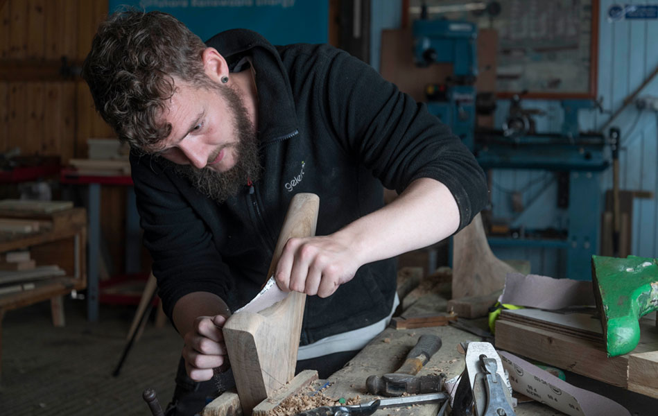 A man in a workshop sanding a piece of wood.