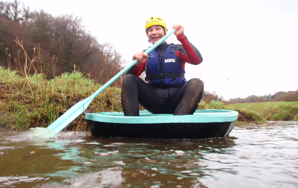 A young man with a paddle in a circular boat on a lake