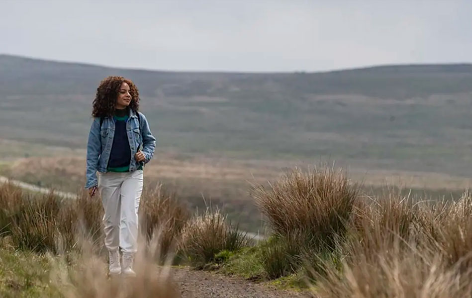 A woman walking along a path in a field with a mountain in the background.