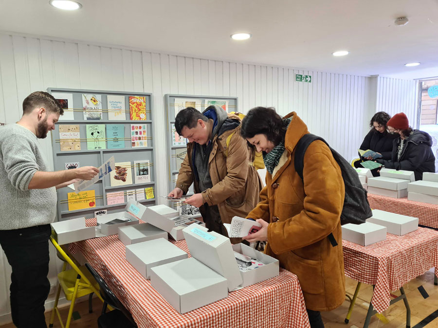 Three people standing around tables looking through boxes of zines