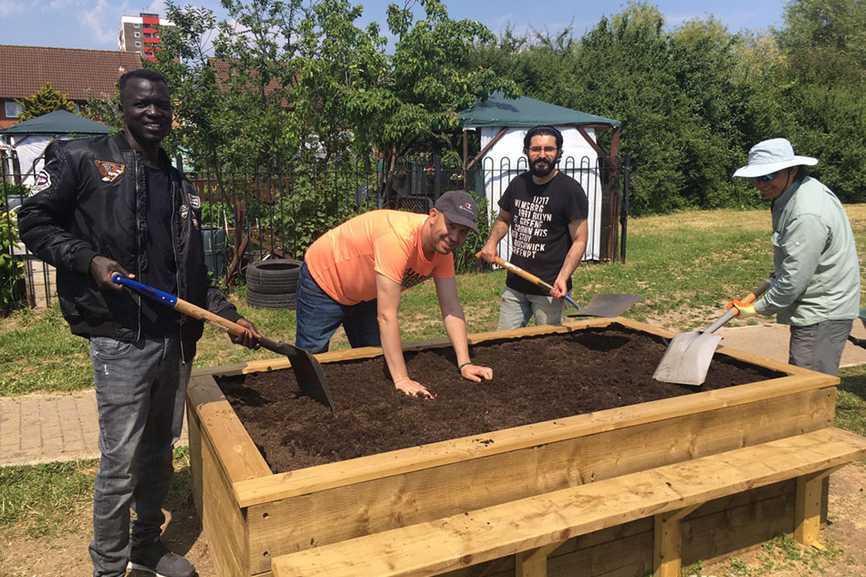 Four men standing around a raised garden bed, smoothing the soil