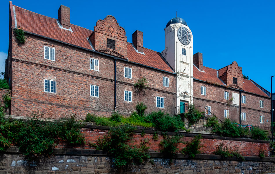 A large red brick building with a white tower featuring a clock at the centre of its length.