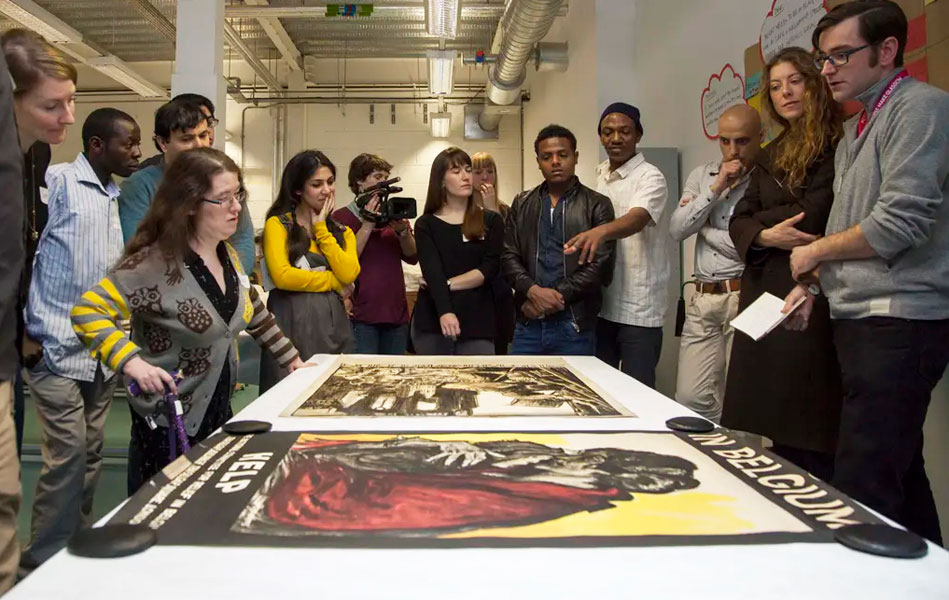 A group of people standing around a table where large posters are laid out.