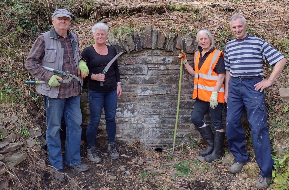 Four people stand in a woodland holding gardening tools