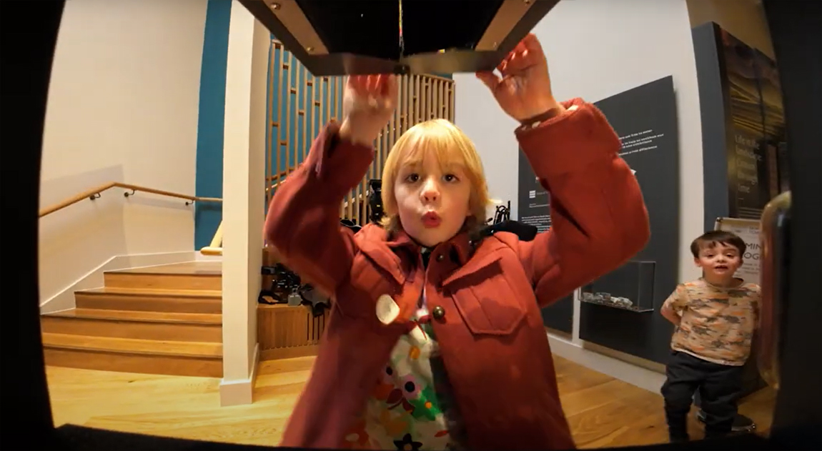 A young boy opening a box at a museum with a 'wow' expression on his face