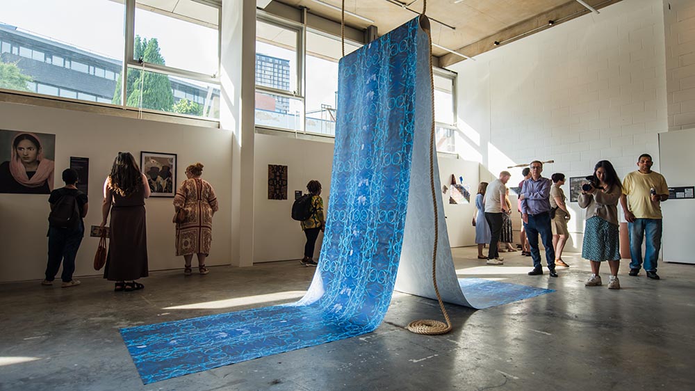 People looking at artwork in a large gallery space. In the foreground is a large work of hanging blue cloth.