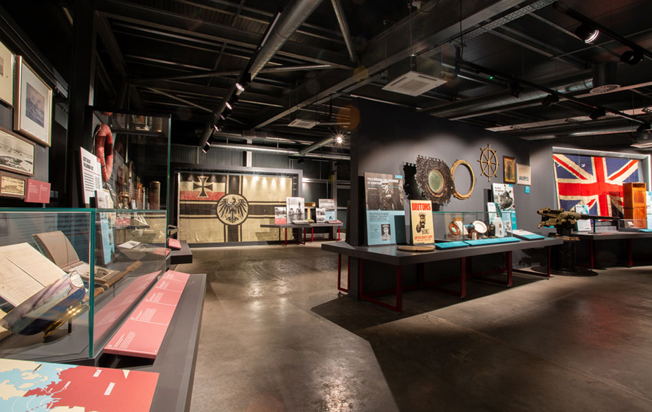 An interior of a museum featuring flags, log books and other artefacts from the First and Second World Wars.