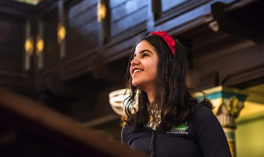A young child in a school uniform looking up and smiling inside a synagogue