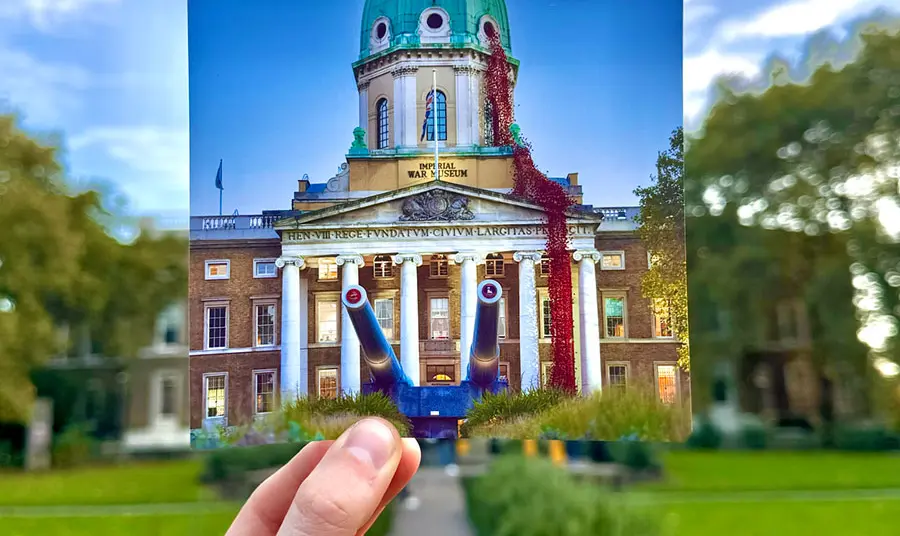 A hand holding a photograph of a domed building with an installation of red poppies flowing from a window in the roof, in front of that same building