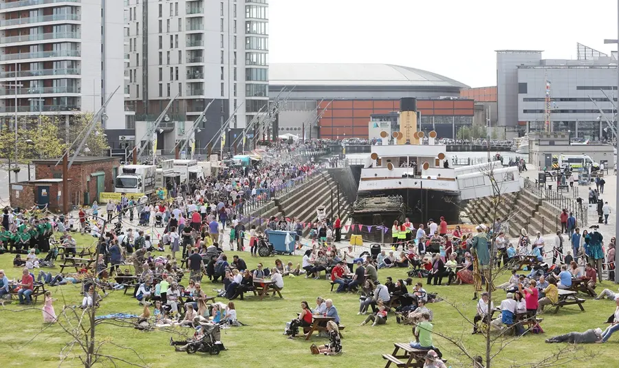 Hundreds of people are gathered, enjoying the sunshine, around a historic ship in dry dock on the Belfast quayside.