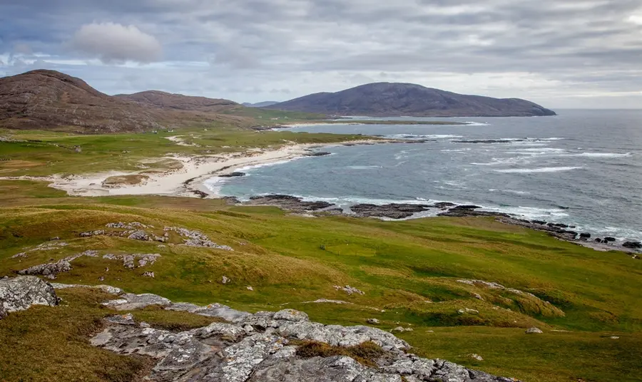 A view looking along the rugged coastline of Barra, towards white sand beaches and distant hills.