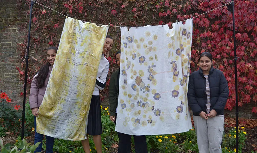 People standing behind a textile artwork made from hanging sheets of fabric printed with text and flowers