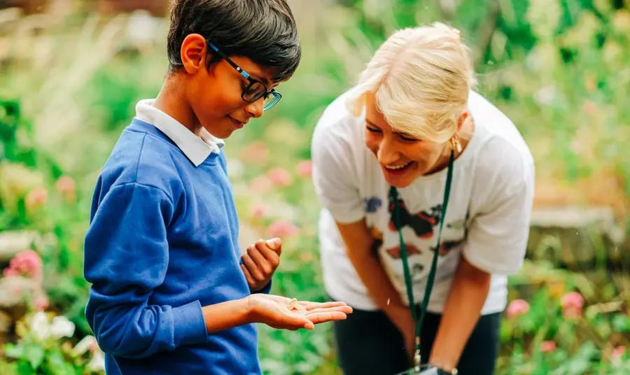 A child holds a butterfly while a guide smiles at him