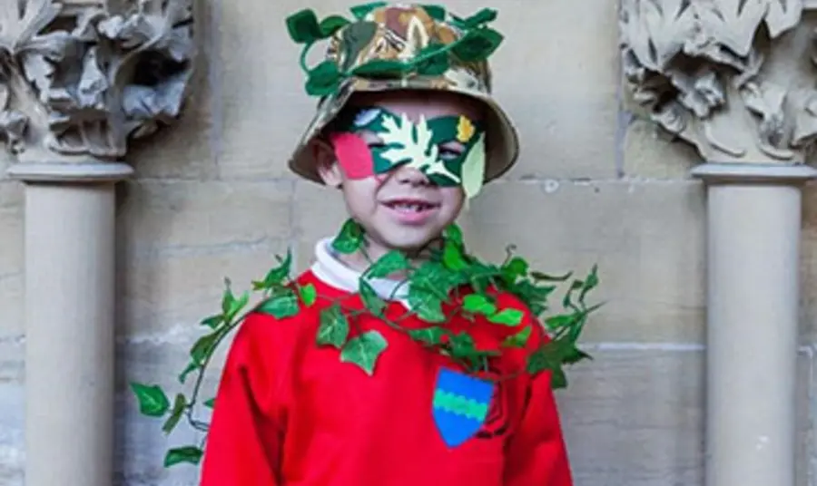 A child in a red jumper, hat and eye mask draped in ivy