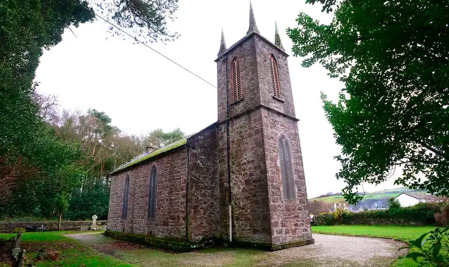 An old stone church with prominent tower, surrounded by grass and trees.