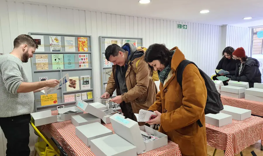 Three people standing around tables looking through boxes of zines