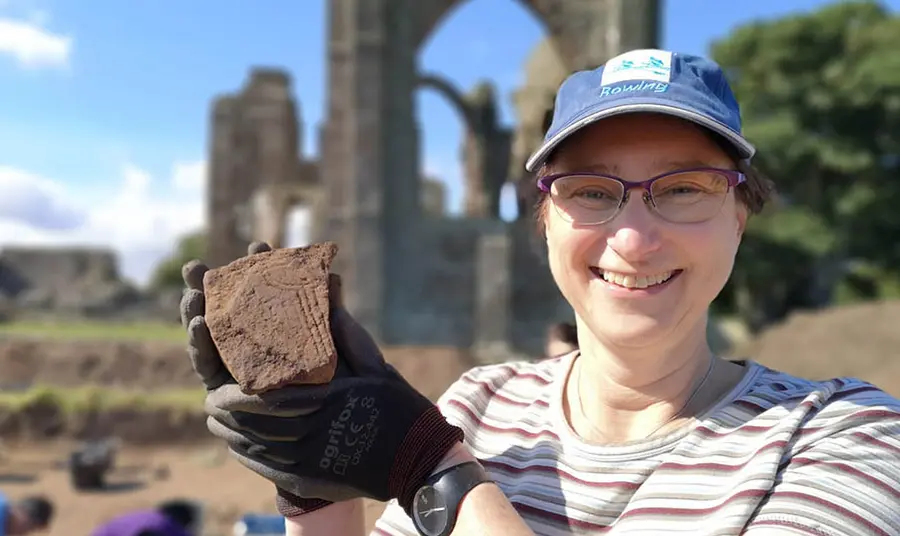 A person at an archaeological dig site holds up a piece of stone which has been excavated