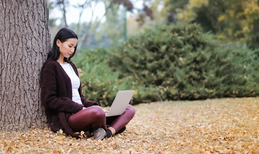 A young woman using a computer laptop under a tree