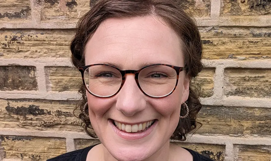 A close-up selfie of a woman with short hair standing against a brick wall