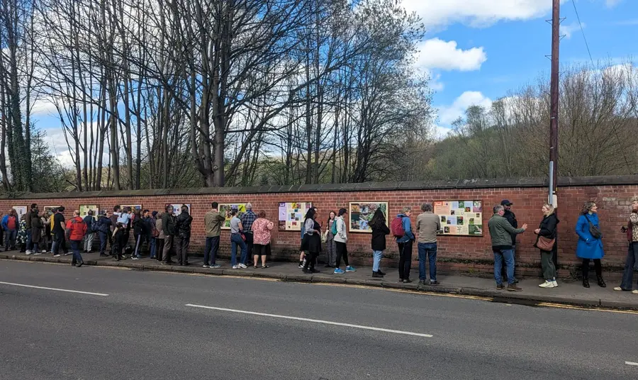 People looking at exhibition panels along a brick wall at the roadside.