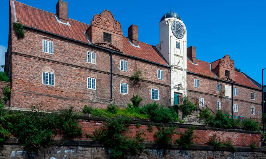 A large red brick building with a white tower featuring a clock at the centre of its length.