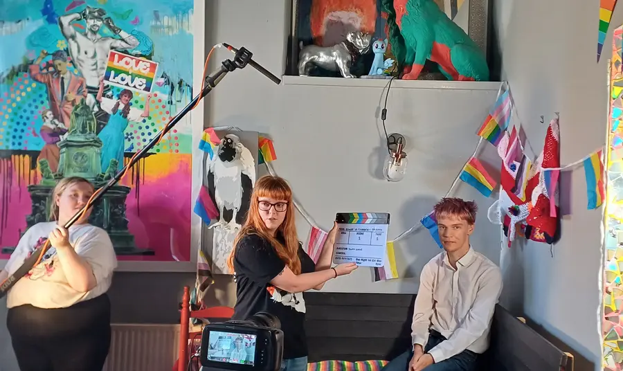 Three young people making a film, one person is holding a microphone, another a clapperboard, and one person is waiting to be interviewed