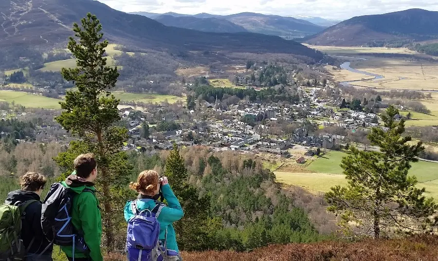 Three people look down over a valley with mountains in the distance