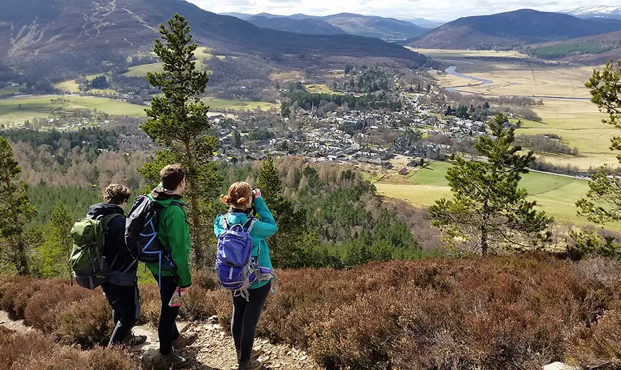 Three people look down over a valley with mountains in the distance