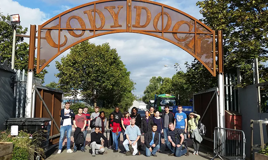 Crowd of people under a rust-coloured metal arch, which reads Cody Dock.