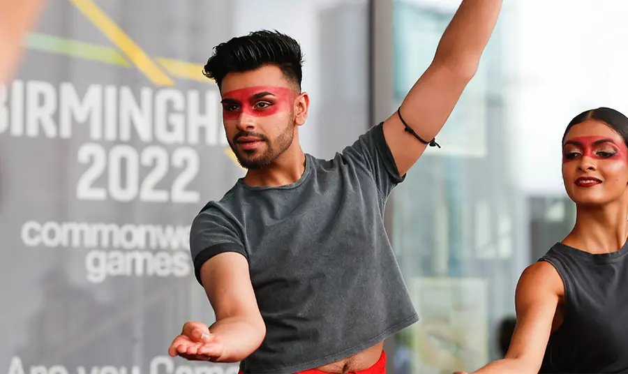 Two people striking a dance pose in front of a 'Commonwealth Games' sign 