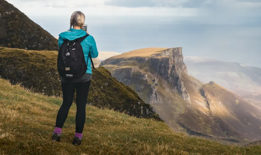 A person standing on a grassy mountainside, looking out to mountains in the distance