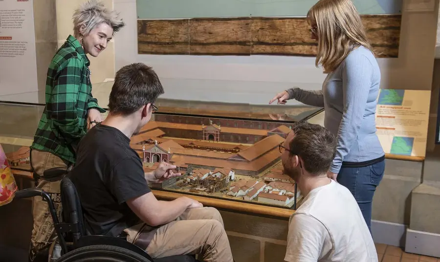 Four young people chatting and looking at a display of a small historical model settlement