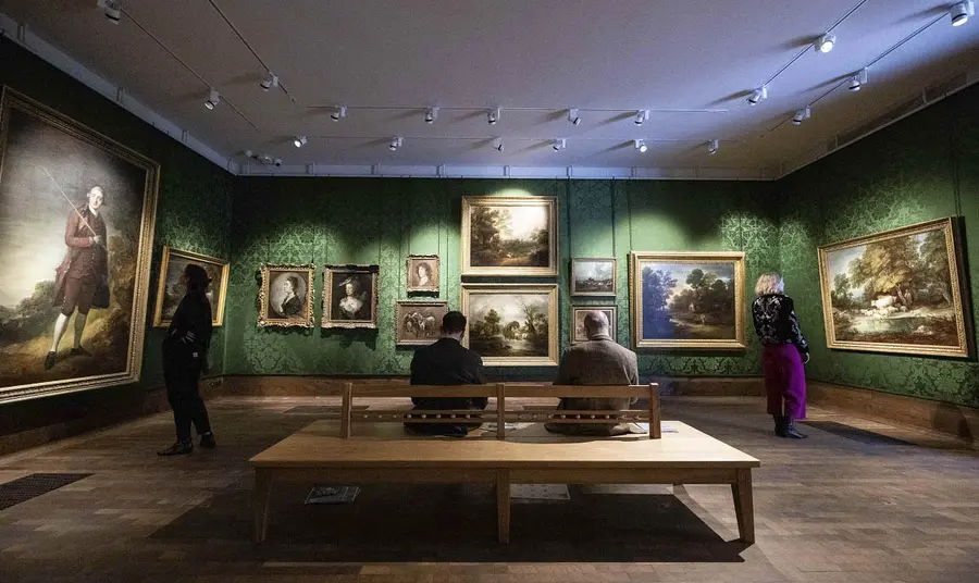 A gallery space with people observing paintings and sitting down 