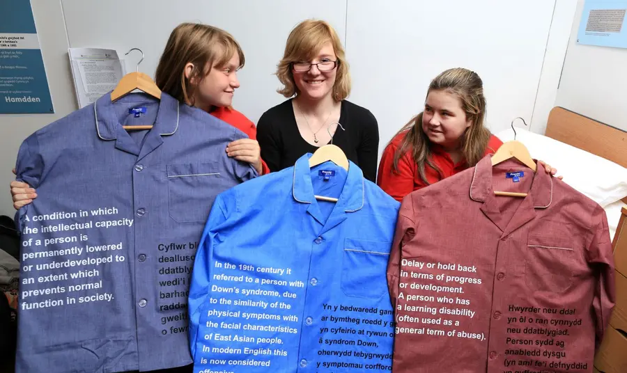 Three participants hold up exhibits including shirts with text written on them