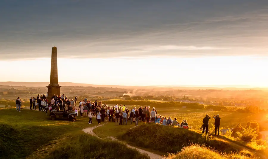 A large group of people stand on top of Ham Hill summit at sunset