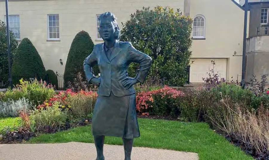 Life-sized statue of a woman in a small, landscaped garden