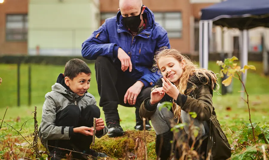 Two school children learning outdoors, watched over by a teacher