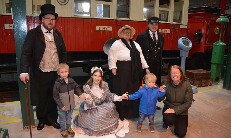 People in period costumes with children in front of an old train