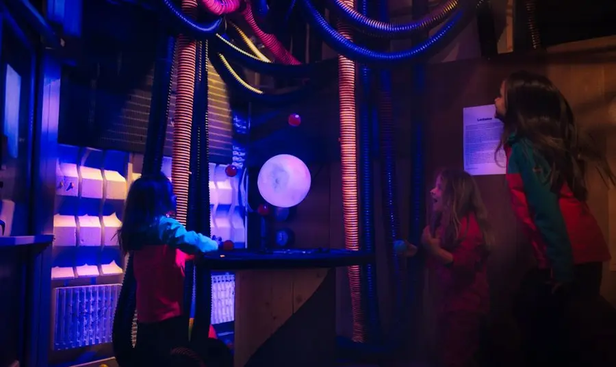 Three children interact with the hovering ball exhibit and balance balls on different air streams