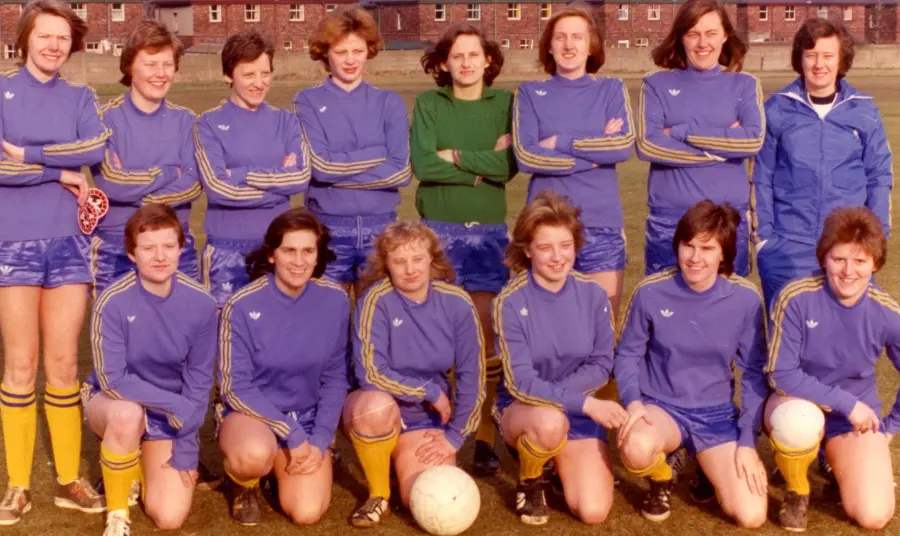 Women's football team face the camera in two rows - one standing behind, one kneeling in front.