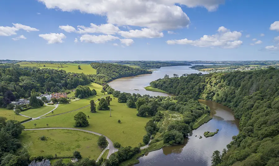 Aerial view over green valley with trees, grass, curving river and blue sky