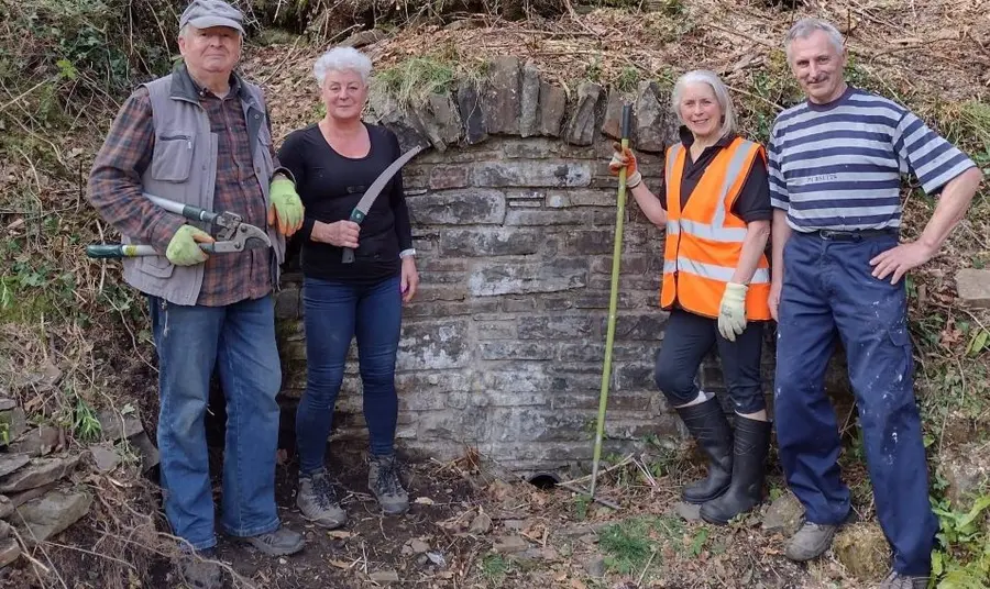 Four people stand in a woodland holding gardening tools