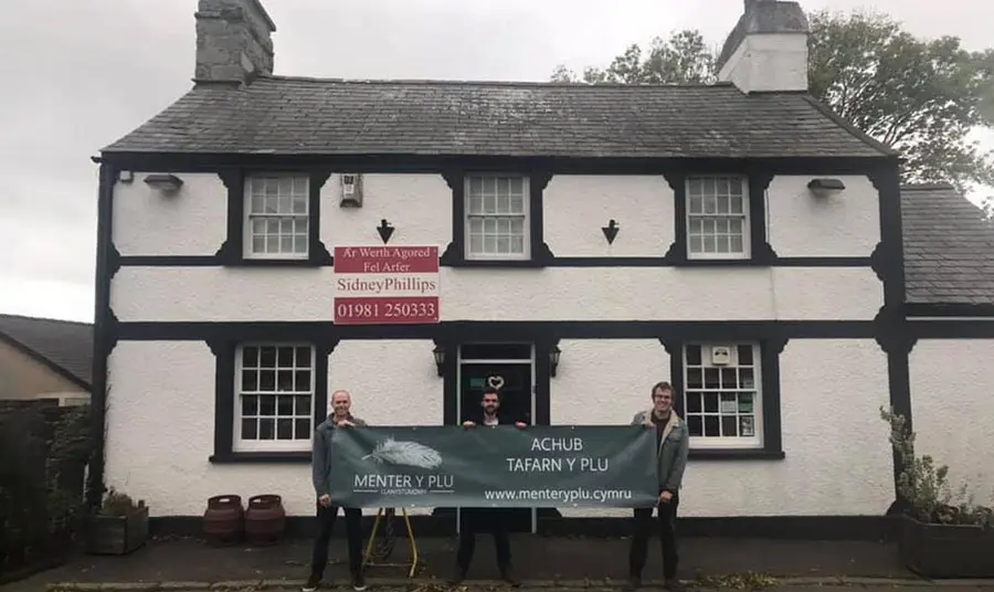 Two people holding a sign for a local community organisation standing outside a historic pub building