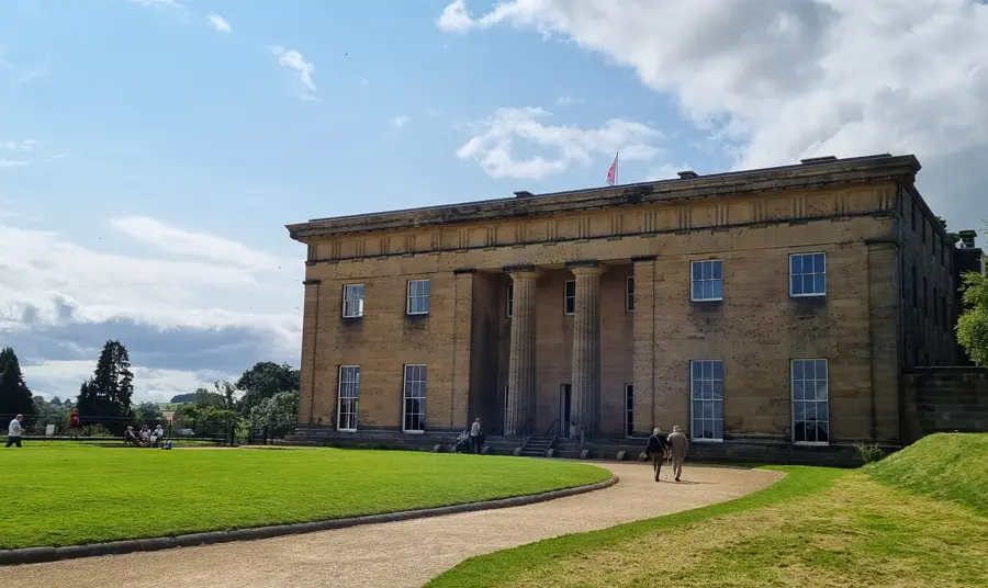 The facade of Belsay Hall on a sunny day, with visitors exploring the grounds