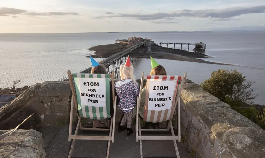 People sitting on deck chairs wearing party hats in front of Birnbeck Pier