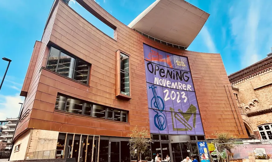 The front of Bristol Beacon is shown with a cafe and seating outside