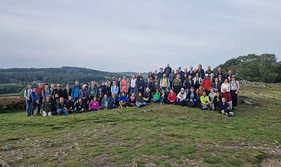 A large group of people wearing outdoor clothing pose for a group photo in the countryside