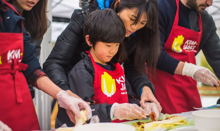 A child in an apron making kimchi with the help of an adult